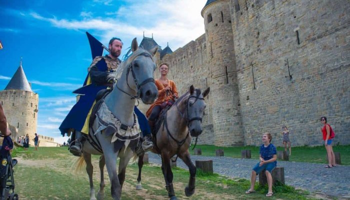 Two people dressed as knights on a horse by a castle in the background.